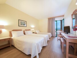 Una habitación de hotel con dos camas, un escritorio, un televisor y una ventana con cortinas.