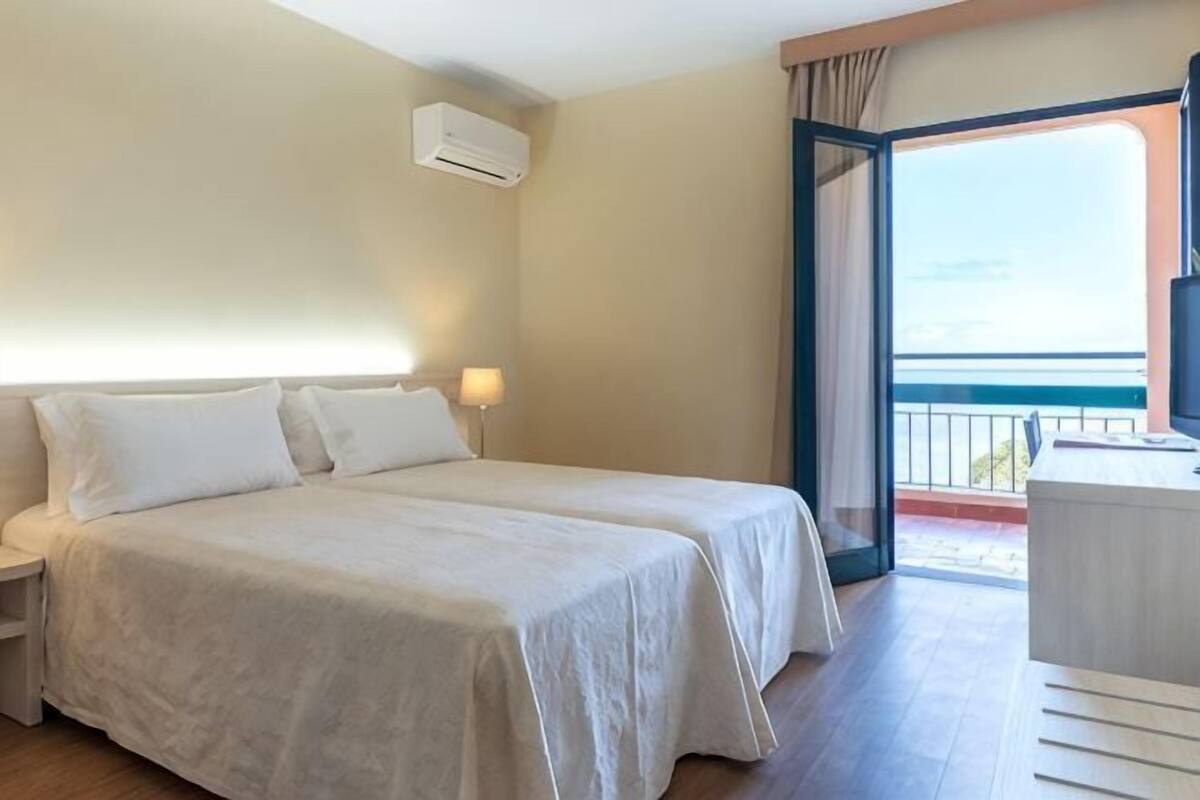 A hotel room with two beds, a balcony, and a TV.