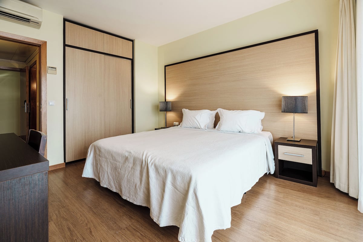 A hotel room with a large bed, a bedside table with a lamp, a wardrobe, and a desk.