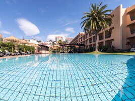 A clear blue pool with tiled flooring, surrounded by lounge chairs and a palm tree.