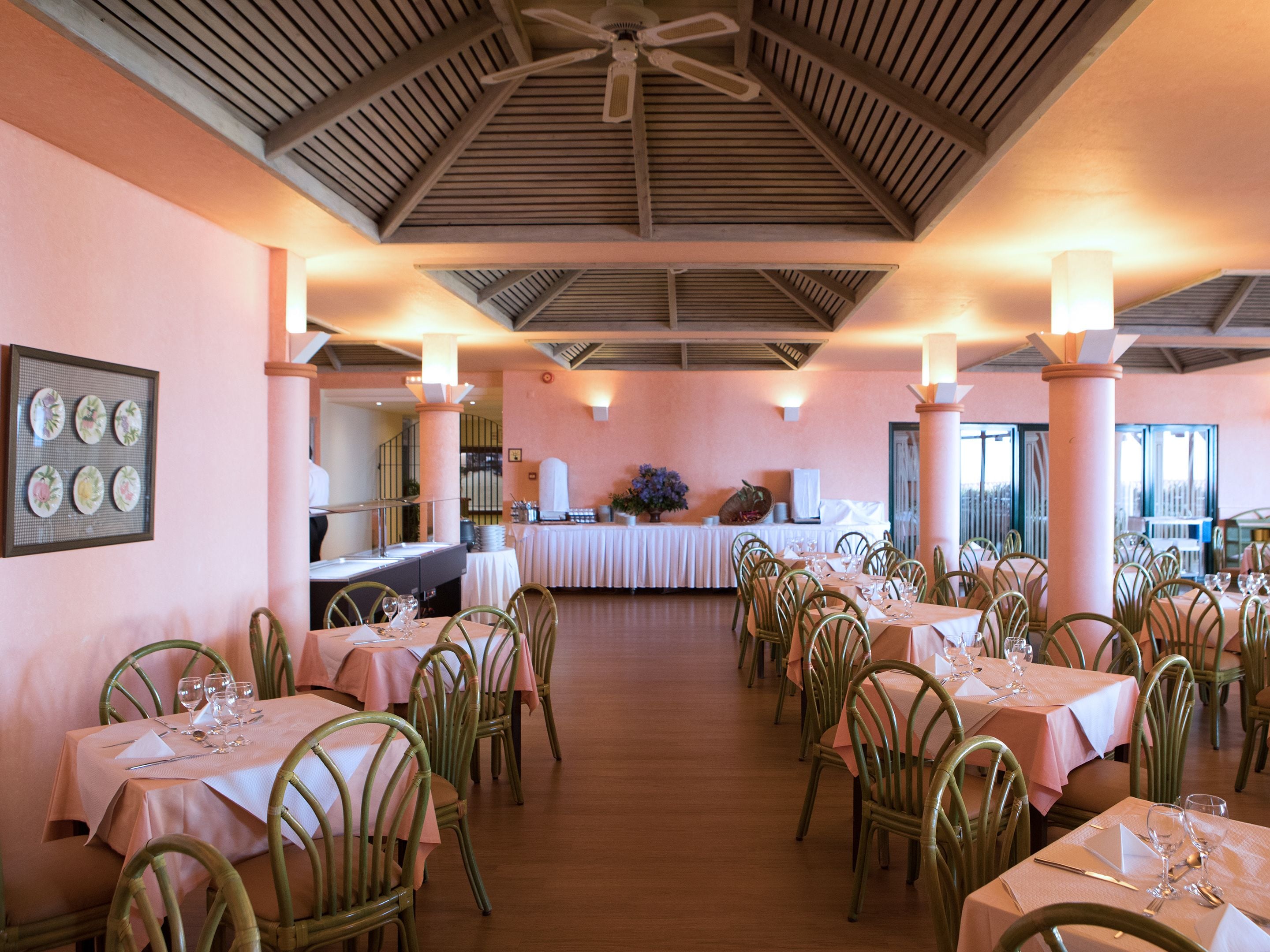 A restaurant with multiple tables and chairs, a ceiling fan, and a large window in the background.