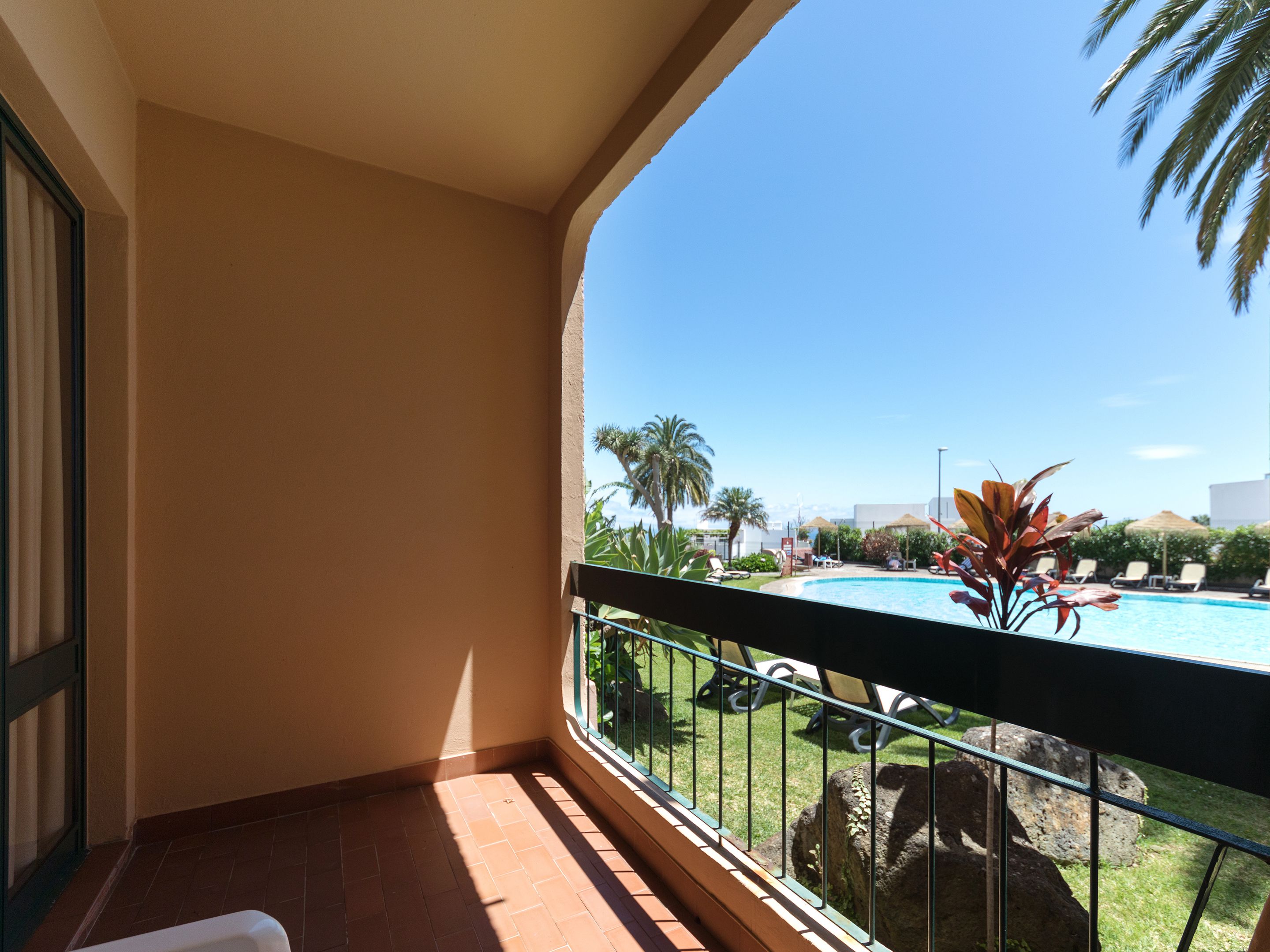 Un balcon avec vue sur une piscine, des palmiers et des chaises longues.