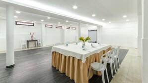 Un salón de conferencias con una larga mesa, sillas blancas y un mantel beige.
