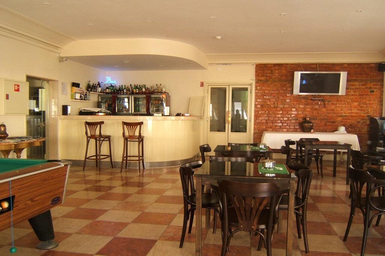 Zona bar con tavolo da biliardo, sgabelli da bar e un bancone pieno di bottiglie. Sono presenti tavoli e sedie per mangiare, e un televisore montato sulla parete in mattoni.