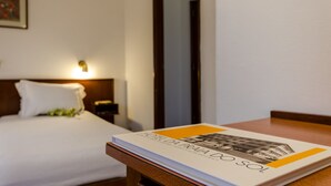 Una habitación de hotel con una cama bien hecha, una mesita de noche con un libro y una lámpara.