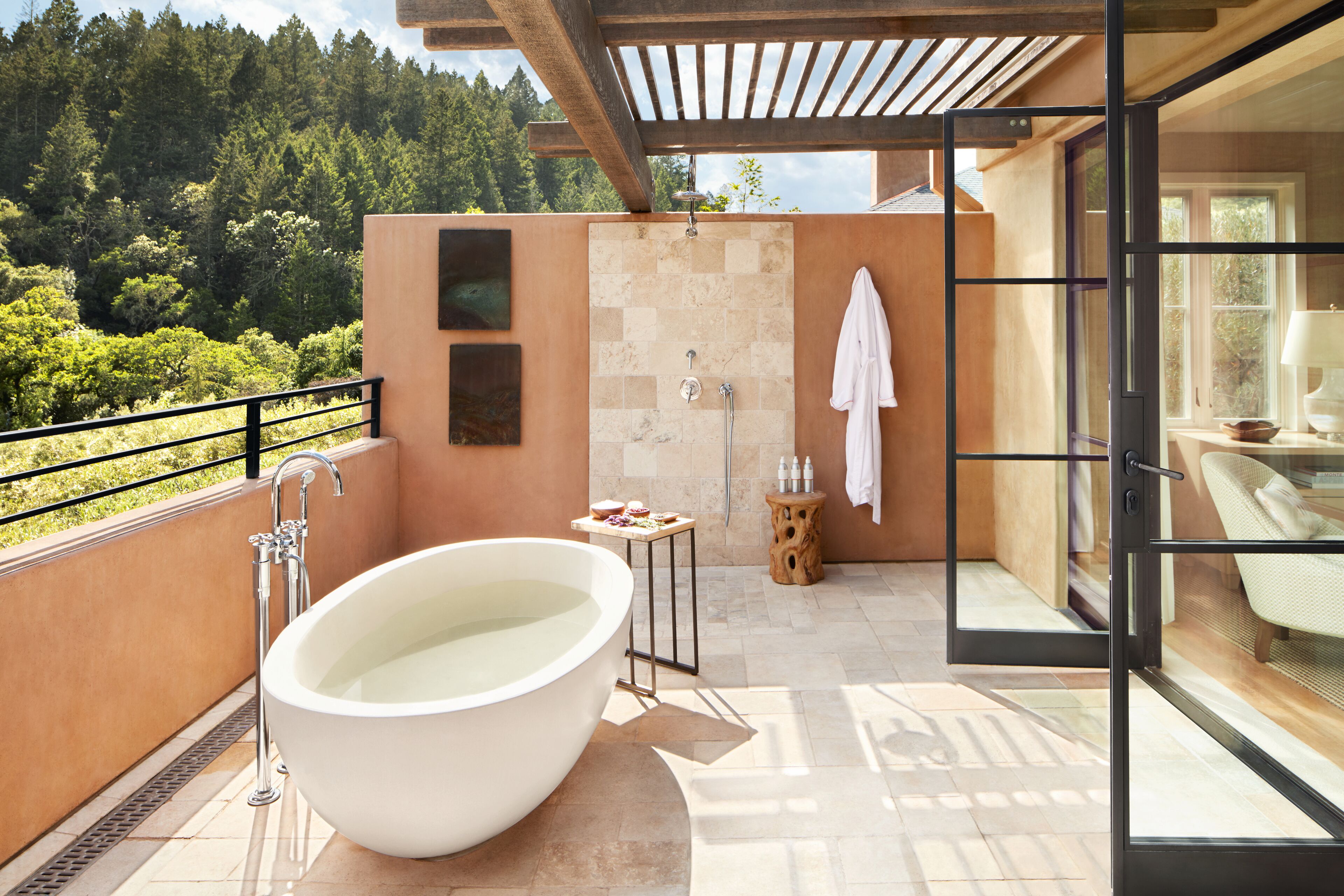 Un baño moderno con una bañera grande, ducha y cabina de ducha con paredes de vidrio. Se observa una mesita con artículos de aseo y un perchero.