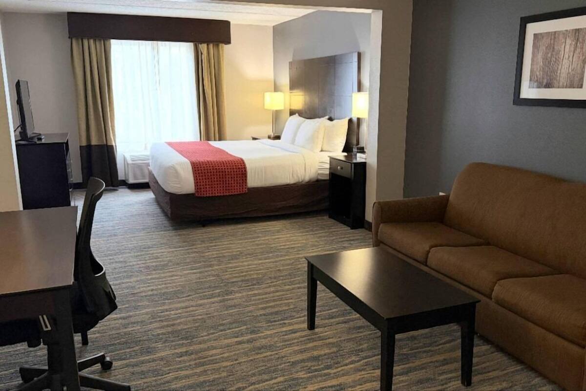 A hotel room with a bed, bedside lamps, a sofa, a desk, and a chair.