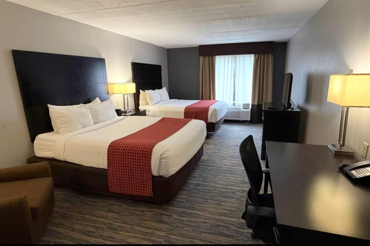 A hotel room with two beds, a desk, a chair, and a TV.