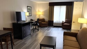 A hotel room with a TV, desk, two armchairs, a sofa, and a lamp. - Comfort Inn & Suites Tampa North I-75 (Tampa)