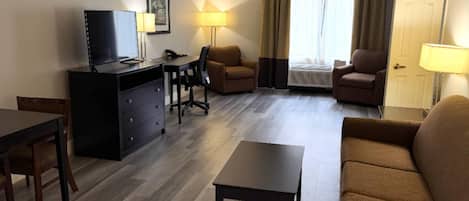 A hotel room with a TV, desk, two armchairs, a sofa, and a lamp.