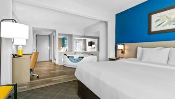 A modern hotel room with a large bed, a desk with a chair, a vanity with a mirror, and a bathtub.