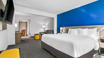 A hotel room with a large bed, a desk, a chair, a TV, and a lamp.