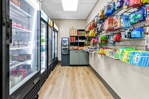 En närbutik med kylfrys på vänster sida, en självbetjäningskassa och hyllor fyllda med snacks och hushållsartiklar.