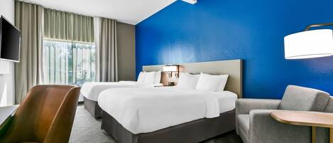 Quarto de hotel com uma cama grande, duas mesas de cabeceira, uma escrivaninha, uma cadeira e uma televisão.