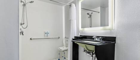 A modern bathroom with a walk-in shower, a white toilet, a sink with a black countertop, and a mirror with a lighted frame.