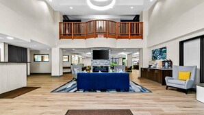 A spacious living area with a high ceiling, a central fireplace, and a dining area with a blue tablecloth. - Comfort Inn & Suites Grand Blanc/Flint (Grand Blanc)