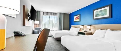 A hotel room with two beds, a desk, a chair, a TV, and a window with curtains.