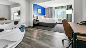A hotel room with a large bathtub, a bed with a headboard, a desk with a chair, and a window with curtains. - Comfort Inn & Suites Grand Blanc/Flint (Grand Blanc)