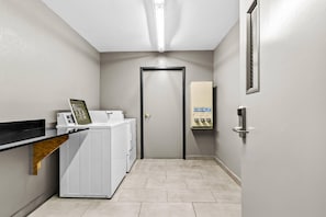 A laundry area with a washing machine, dryer, and a utility panel. - Comfort Inn & Suites Grand Blanc/Flint (Grand Blanc)
