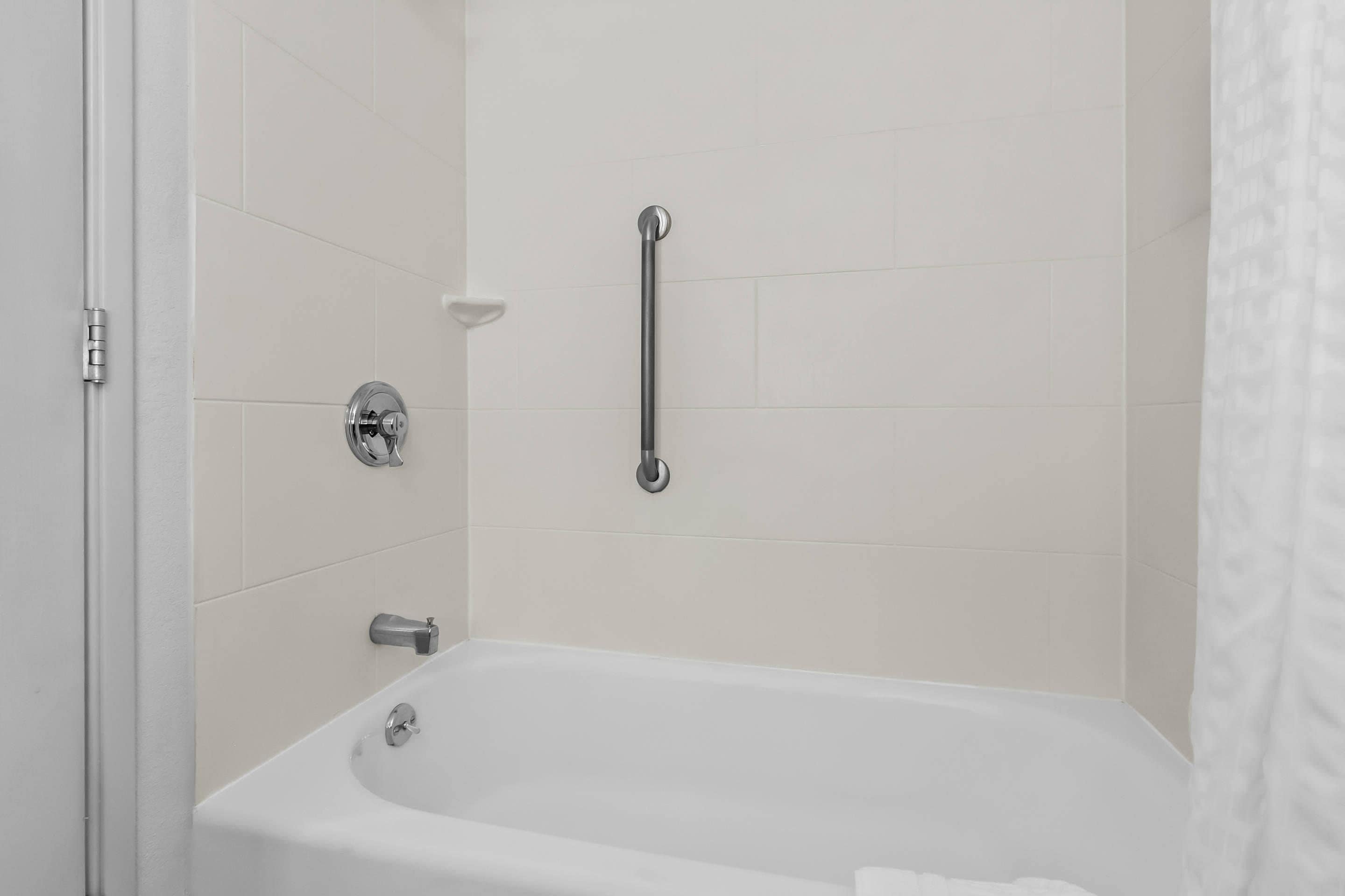 A modern bathroom with a white bathtub, a handheld showerhead, and a grab bar.