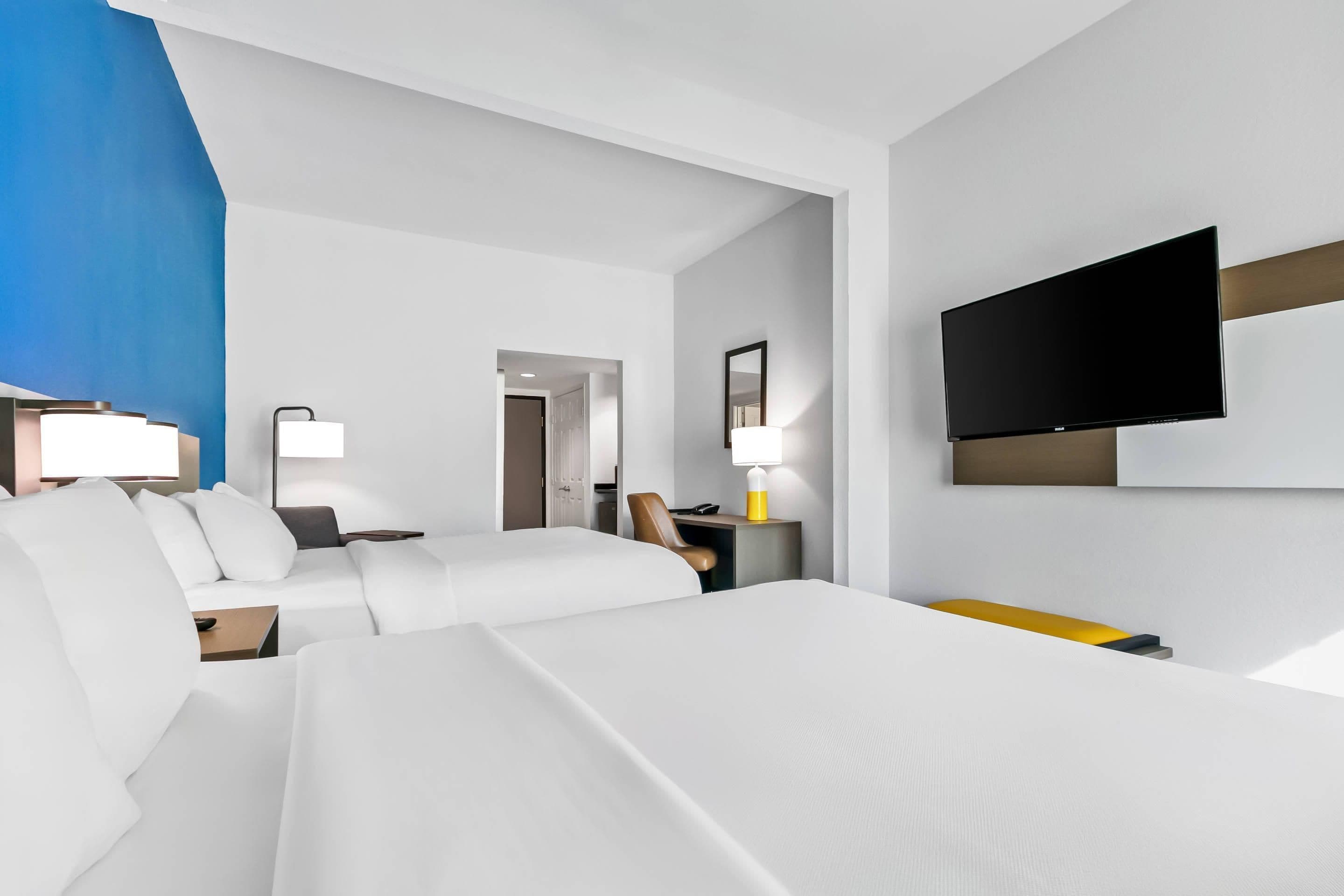Habitación de hotel con una cama grande, un televisor montado en la pared y un escritorio con lámpara.