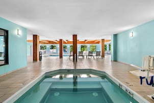 Una piscina interior con agua cristalina, pilares de madera y sillones de descanso.