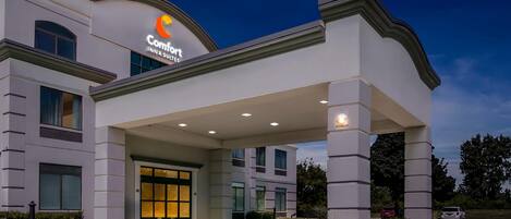 A hotel entrance with a large canopy, a sign reading 'Comfort Inn & Suites,' and a well-lit driveway.