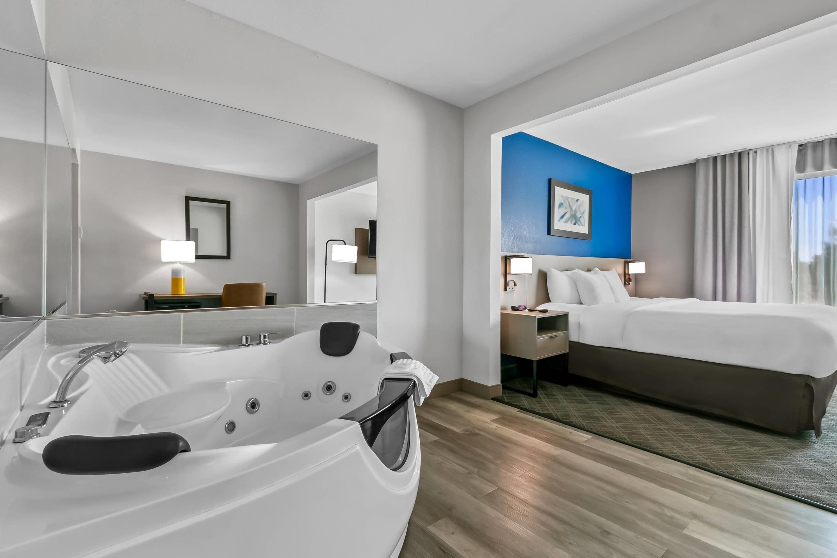 Quarto de hotel com uma banheira grande, uma cama, uma mesinha de cabeceira e uma parede azul decorativa.