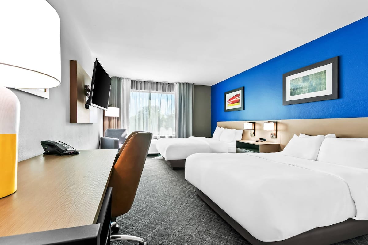 A hotel room with two beds, a desk, a chair, a TV, and a window with curtains.