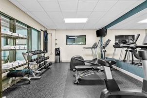 Un gimnasio con equipo de ejercicio, cinta de correr y soporte para pesas.