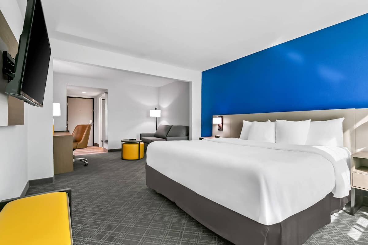 A hotel room with a large bed, a desk, a chair, a TV, and a lamp.