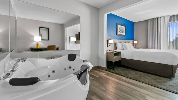 A modern hotel room with a large bathtub, a bed, a desk, and a nightstand. - Comfort Inn & Suites Grand Blanc/Flint (Grand Blanc)