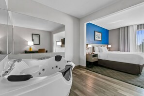 A modern hotel room with a large bathtub, a bed, a desk, and a nightstand.