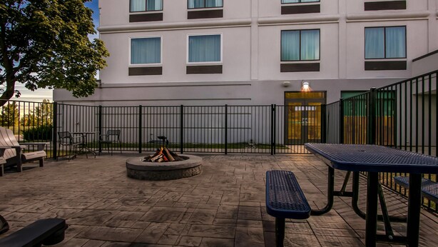 An outdoor patio with stone flooring, a fire pit, and metal tables and benches. - Comfort Inn & Suites Grand Blanc/Flint (Grand Blanc)