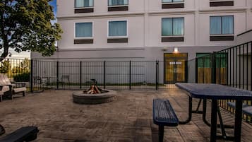 Eine Terrasse im Freien mit Steinböden, einem Feuerkorb und Metalltischen und -bänken.