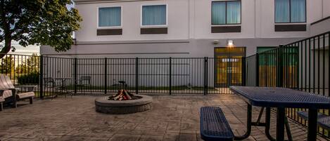 Un patio al aire libre con piso de piedra, una fogata y mesas y bancos de metal.