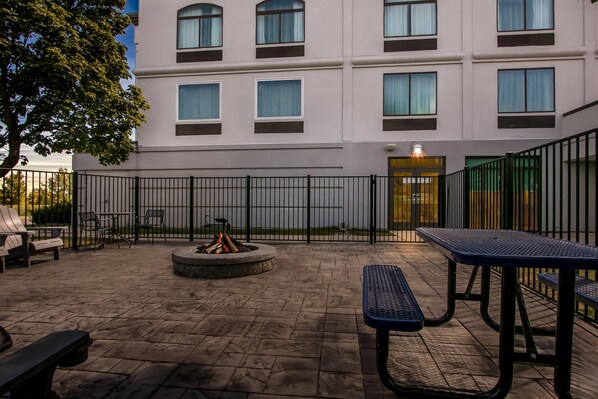 An outdoor patio with stone flooring, a fire pit, and metal tables and benches.