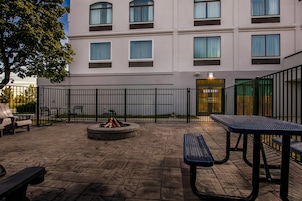 Un patio al aire libre con piso de piedra, una fogata y mesas y bancos de metal.