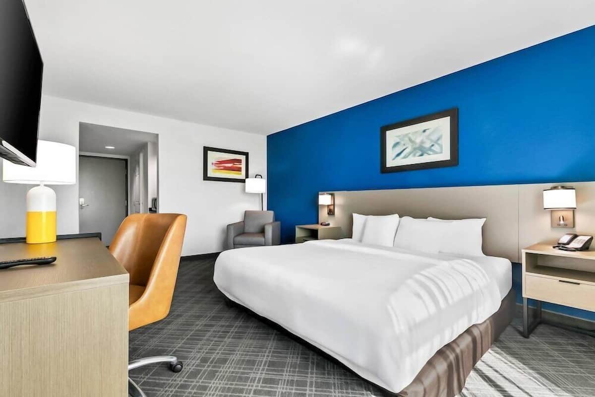 A hotel room with a large bed, a desk, a chair, and a TV.