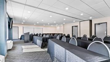 A conference room with long tables and chairs, a projector screen, and a whiteboard.