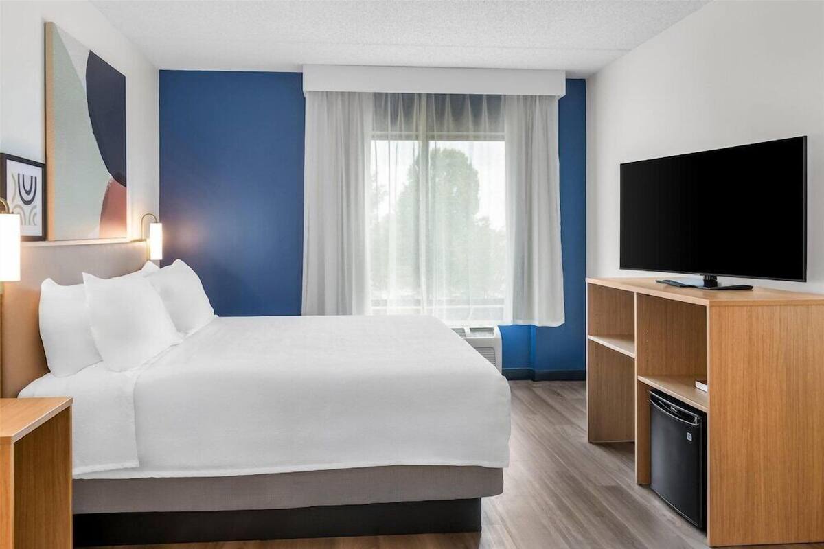 Une chambre d’hôtel avec un lit, une télévision, un bureau et une fenêtre avec des rideaux.