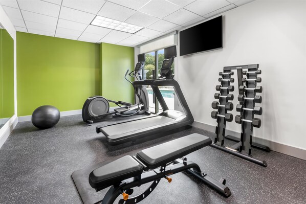 Un gimnasio con cintas de correr, un banco para press de banca, una máquina de remo y un juego de pesas.