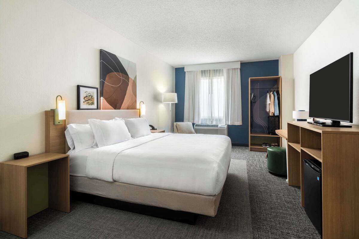 Une chambre d’hôtel avec un grand lit, des tables de chevet, une télévision, une armoire et une fenêtre avec des rideaux.