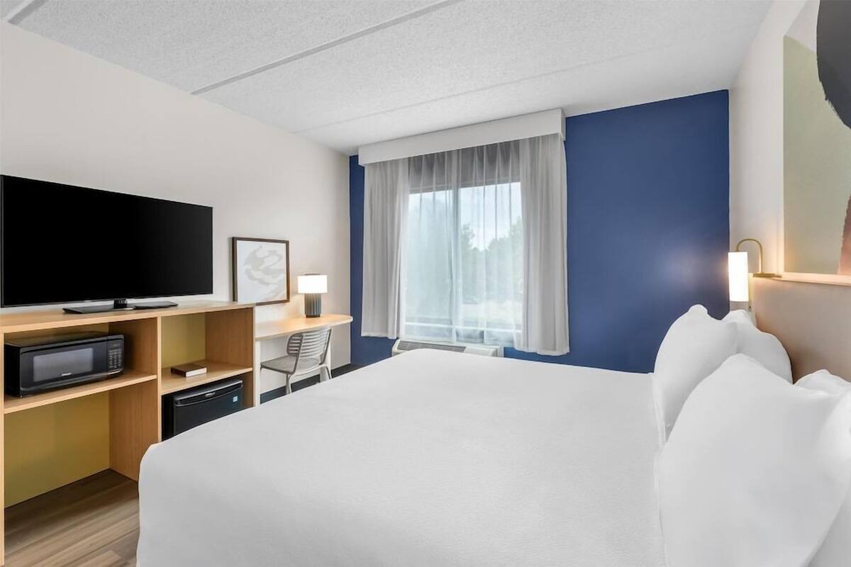 Une chambre d’hôtel équipée d’un lit, d’une télévision, d’un bureau avec une chaise, d’un four à micro-ondes et d’une fenêtre avec des rideaux.