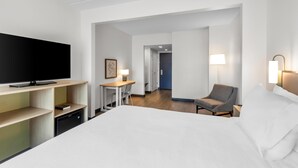 Una habitación de hotel con cama, escritorio, silla, televisor y lámpara.