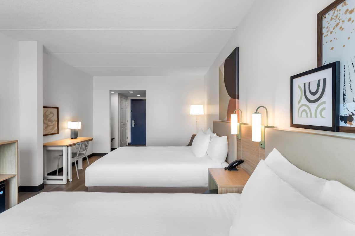 Une chambre d’hôtel avec deux lits, un bureau et une chaise. Une porte donne accès à une autre pièce.