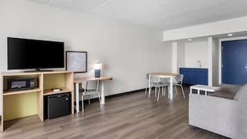 Una sala de estar moderna con televisión de pantalla plana, un refrigerador compacto, una mesa de comedor con sillas y un sofá.