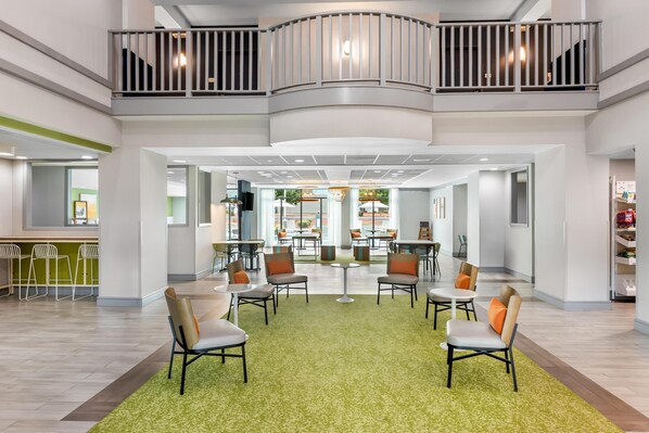 A spacious lobby with a green carpet, seating area, and a balcony with railings.
