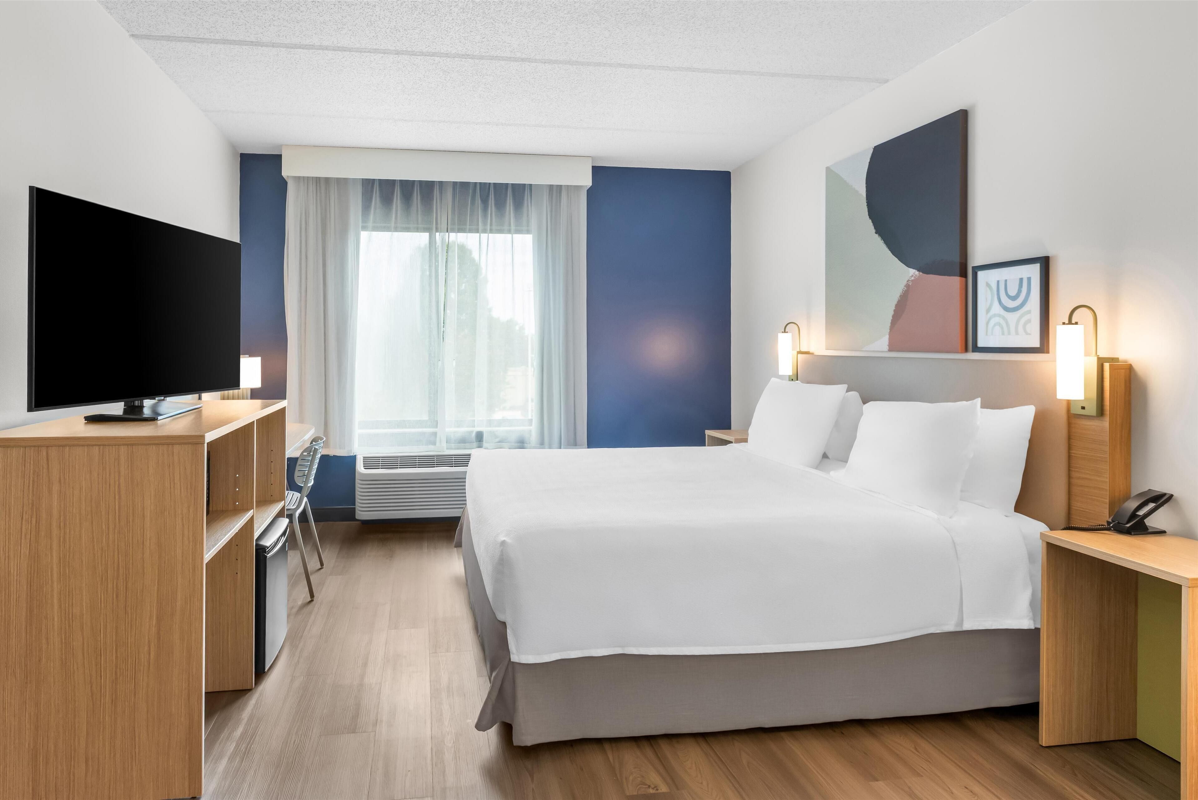 A modern hotel room with a large bed, a flat-screen TV, a desk, and a chair.