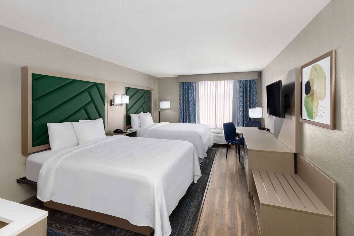 A hotel room with two beds, a desk, a TV, and a window with curtains.